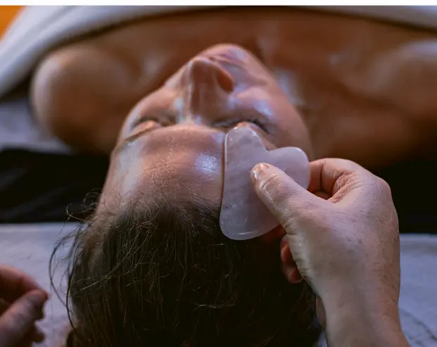 Close-up of a relaxing facial treatment using a gua sha stone on a person's forehead, with a calm and soothing atmosphere.