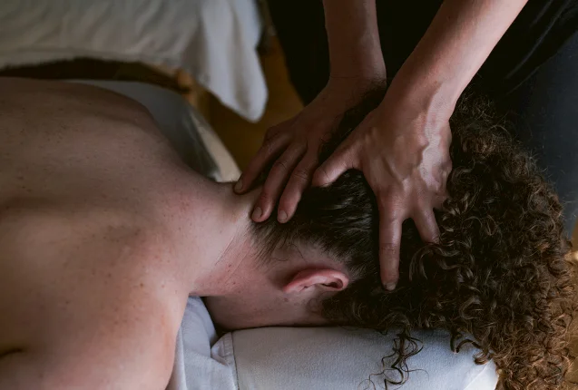 Close-up of a therapist's hands providing a soothing head and neck massage to a client lying face down in a calm and serene spa setting.